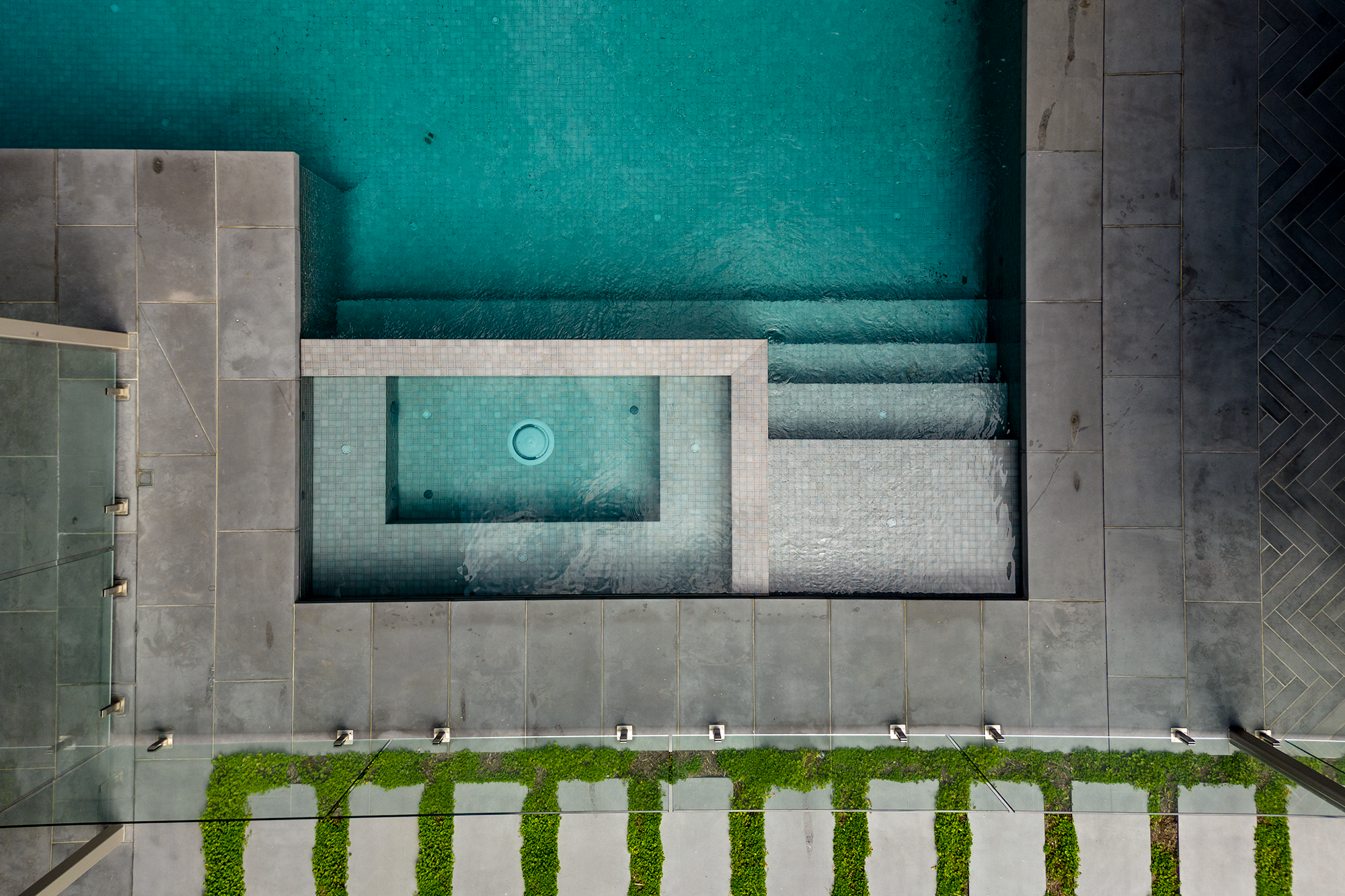 Vertical drone aerial photography of a luxury swimming pool in Melbourne, featuring custom green tiling, minimalist concrete surrounds, and architectural landscape geometry.
